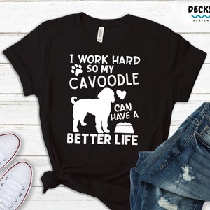 May include: Black t-shirt featuring a white silhouette of a Cavoodle dog and the text "I work hard so my Cavoodle can have a better life".