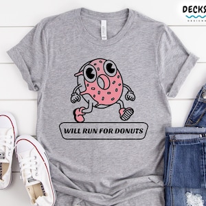Puede incluir: Una camiseta gris con un donut de dibujos animados corriendo y el texto "WILL RUN FOR DONUTS".