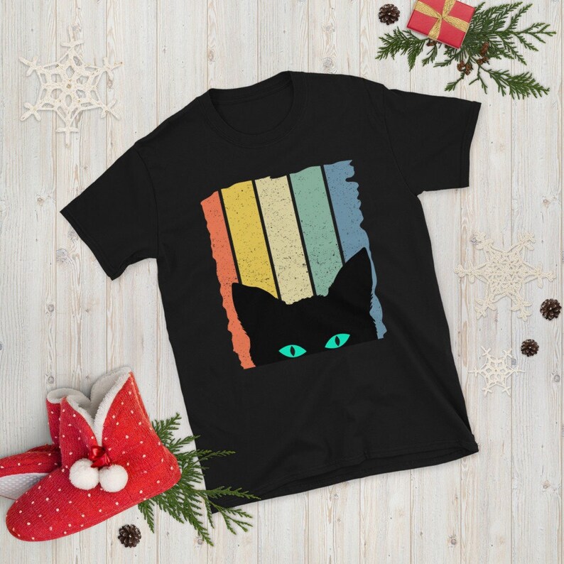 May include: Black t-shirt with a retro-style graphic of a black cat peeking out from behind colorful stripes. The cat's eyes are green.