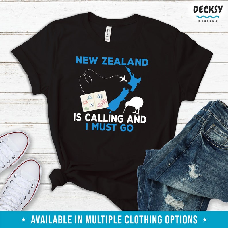 May include: Black t-shirt with a blue and white graphic of New Zealand, a kiwi bird, and a passport. The text "New Zealand is calling and I must go" is printed on the shirt.