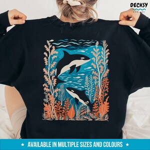 May include: Black sweatshirt with a graphic print of two orcas swimming in a blue ocean with coral and seaweed. The text "AVAILABLE IN MULTIPLE SIZES AND COLORS" is printed at the bottom of the image.