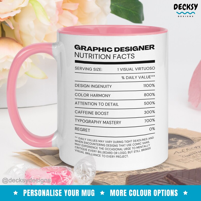 May include: A white ceramic mug with a pink rim and handle. The mug features a graphic design nutrition facts label with the text "Graphic Designer Nutrition Facts" and a list of design elements with their percentage daily value. The text at the bottom of the mug reads "Personalise Your Mug More Colour Options".