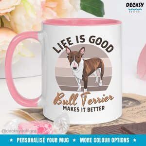 May include: White ceramic mug with a pink rim and handle. The mug features a brown and white bull terrier dog illustration with a sunset background. The text "Life is good Bull Terrier makes it better" is printed on the mug.