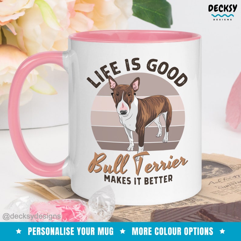 May include: White ceramic mug with a pink rim and handle. The mug features a brown and white bull terrier dog illustration with a sunset background. The text "Life is good Bull Terrier makes it better" is printed on the mug.