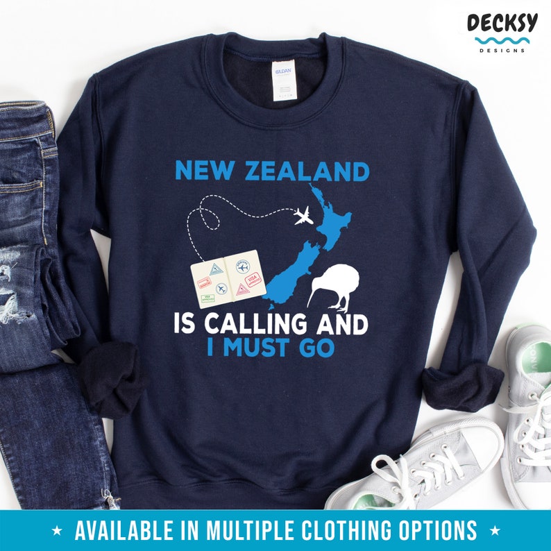 May include: Navy blue sweatshirt with a graphic design of a map of New Zealand, a kiwi bird, and a passport with stamps. The text "New Zealand is calling and I must go" is printed on the sweatshirt.