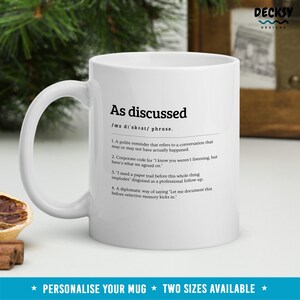Peut inclure: Mug en c&eacute;ramique blanche avec le texte "As discussed" et une d&eacute;finition. La tasse a une anse et est plac&eacute;e sur un fond flou. Le bas de la tasse porte le texte "Personalise your mug * Two sizes available *".