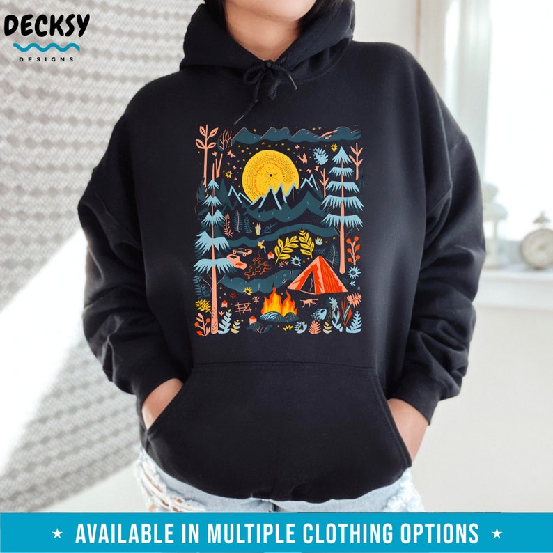 May include: Black hoodie with a colorful illustration of a camping scene with a tent, campfire, mountains, and a full moon. The illustration is surrounded by a frame of trees and flowers.