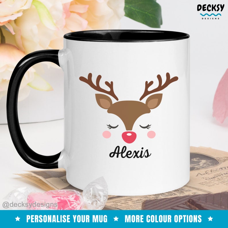 Op de afbeelding: Witte keramische mok met een zwarte rand. De mok heeft een cartoon rendiergezicht met gesloten ogen en een rode neus. De naam "Alexis" staat onder het rendiergezicht gedrukt.
