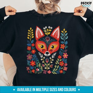 K&ouml;nnte beinhalten: Schwarzer Pullover mit einem bunten Fuchs-Design mit floralen Mustern in Rot, Gelb, Gr&uuml;n, Blau und Lila. Der Fuchs hat ein rotes Gesicht mit gelben Augen und einer schwarzen Nase.
