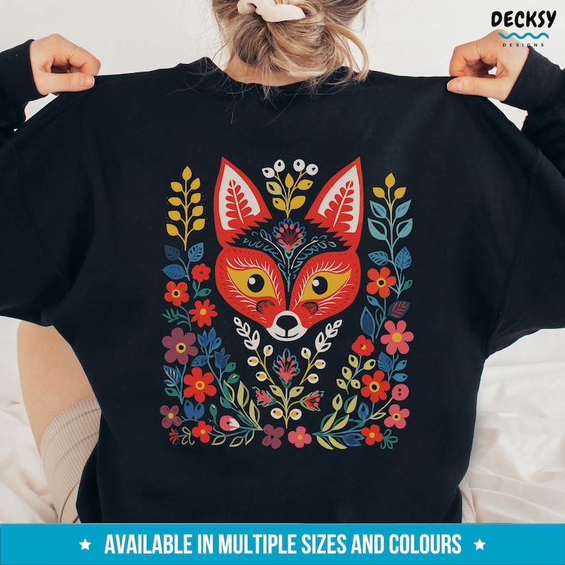 K&ouml;nnte beinhalten: Schwarzer Pullover mit einem bunten Fuchs-Design mit floralen Mustern in Rot, Gelb, Gr&uuml;n, Blau und Lila. Der Fuchs hat ein rotes Gesicht mit gelben Augen und einer schwarzen Nase.