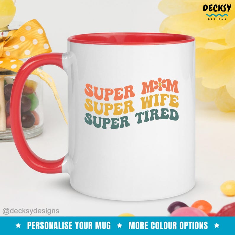 K&ouml;nnte beinhalten: Wei&szlig;e Keramiktasse mit rotem Rand und Henkel. Die Tasse hat ein Retro-Design mit dem Text "SUPER MOM SUPER WIFE SUPER TIRED" in bunten, &uuml;bereinanderliegenden Buchstaben.