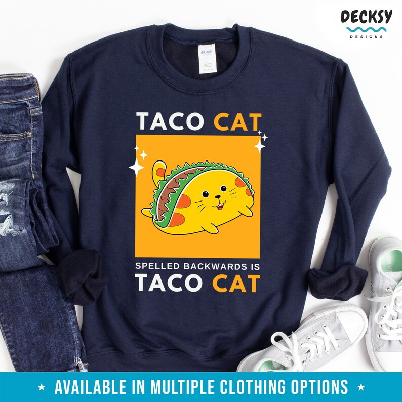 May include: A navy blue sweatshirt with the text "TACO CAT" in white letters. A cartoon cat wearing a taco is inside a yellow rectangle. The text "SPELLED BACKWARDS IS TACO CAT" is below the rectangle.