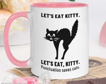 May include: White ceramic mug with a pink rim. The mug features a black silhouette of a cat with the text "Let's Eat Kitty. Let's Eat, Kitty. Punctuation saves cats."
