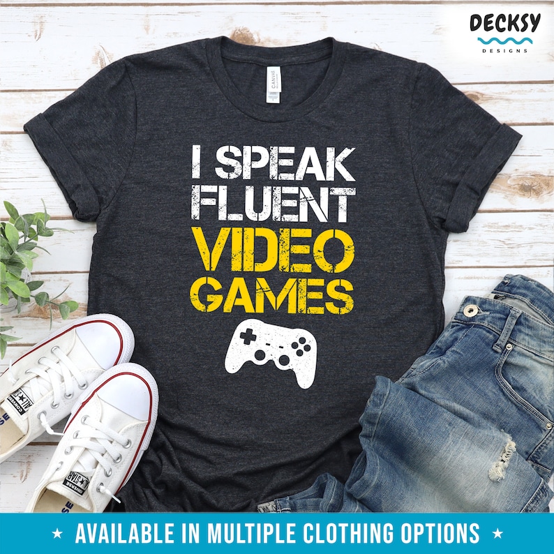 May include: A dark gray t-shirt with the text "I SPEAK FLUENT VIDEO GAMES" in yellow with a white video game controller graphic.