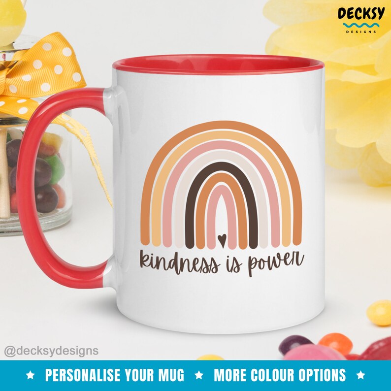 May include: White ceramic mug with a red rim and handle. The mug features a rainbow design with brown, orange, and pink colors. The text "kindness is power" is printed below the rainbow.