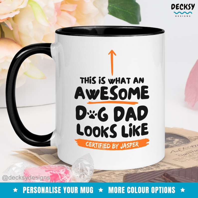 May include: White ceramic mug with a black rim and handle. The mug has an orange arrow pointing up and the text "This is what an awesome Dog Dad looks like. Certified by Jasper."