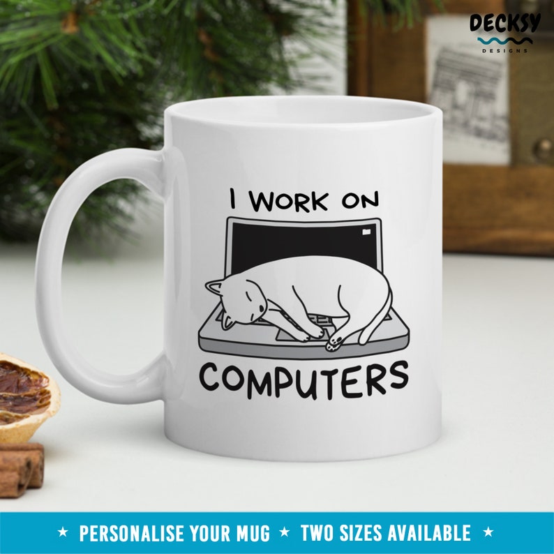 May include: White ceramic mug with a black and white illustration of a cat sleeping on a laptop. The text "I work on computers" is printed on the mug.