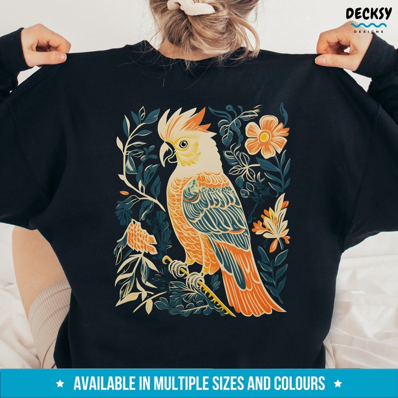 May include: A black sweatshirt featuring a colourful illustration of a cockatoo bird perched on a branch surrounded by flowers and leaves.