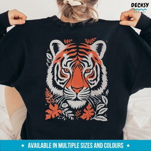 Puede incluir: Sudadera negra con una ilustraci&oacute;n colorida de la cara de un tigre rodeada de follaje. El tigre tiene rayas naranjas y blancas y una nariz negra.