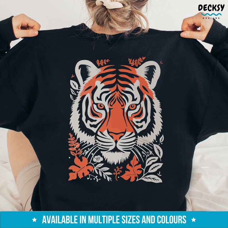 Puede incluir: Sudadera negra con una ilustraci&oacute;n colorida de la cara de un tigre rodeada de follaje. El tigre tiene rayas naranjas y blancas y una nariz negra.