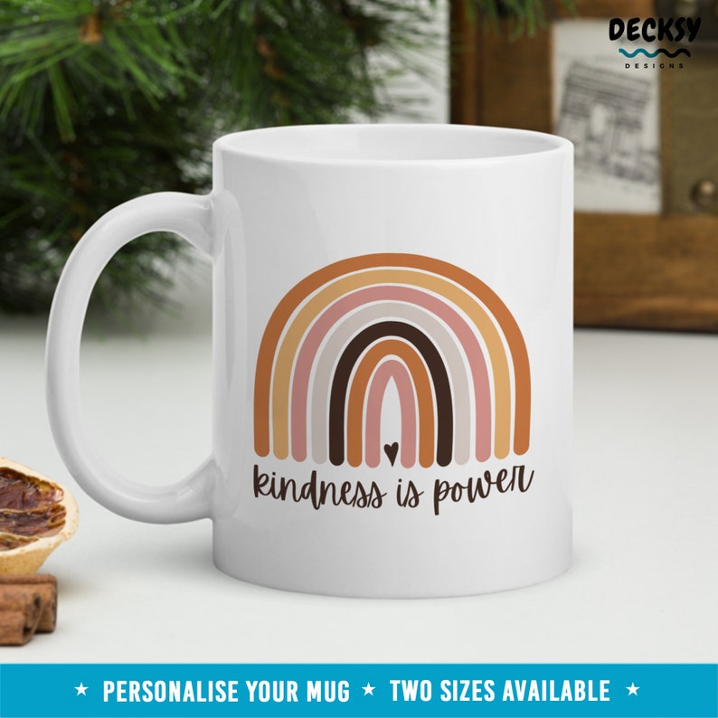 May include: White ceramic mug with a rainbow design in shades of brown, pink, and gray. The text "kindness is power" is printed below the rainbow. A small heart is in the center of the rainbow.