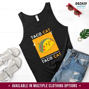 May include: Black tank top with a yellow and orange illustration of a cat holding a taco. The text "Taco Cat" is written in white letters above the cat and "Spelled backwards is Taco Cat" is written in white letters below the cat.