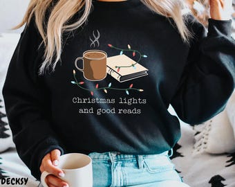 May include: A black sweatshirt with a graphic design of a cup of hot chocolate, a book, and Christmas lights. The text "Christmas lights and good reads" is printed below the graphic.