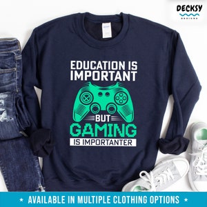 K&ouml;nnte beinhalten: Ein marineblauer Pullover mit dem Text "Education is important but gaming is importanter" in Wei&szlig;. Eine gr&uuml;ne Grafik eines Videospiel-Controllers befindet sich in der Mitte des Textes.
