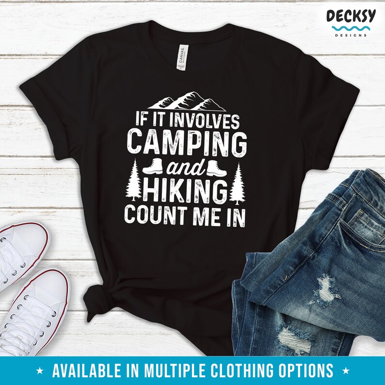 May include: Black t-shirt with white text that reads "If it involves camping and hiking count me in". The text is surrounded by a mountain range and hiking boots.