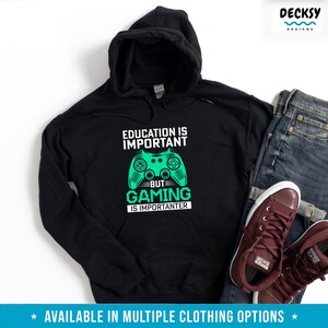 K&ouml;nnte beinhalten: Schwarzer Kapuzenpullover mit einem gr&uuml;nen Videospiel-Controller-Motiv und dem Text "Bildung ist wichtig, aber Gaming ist wichtiger".