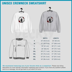 May include: White and grey unisex crewneck sweatshirts. Each sweatshirt features a graphic of a black crow perched in a wreath of branches and red roses. The image includes a size chart with measurements in inches and centimeters.