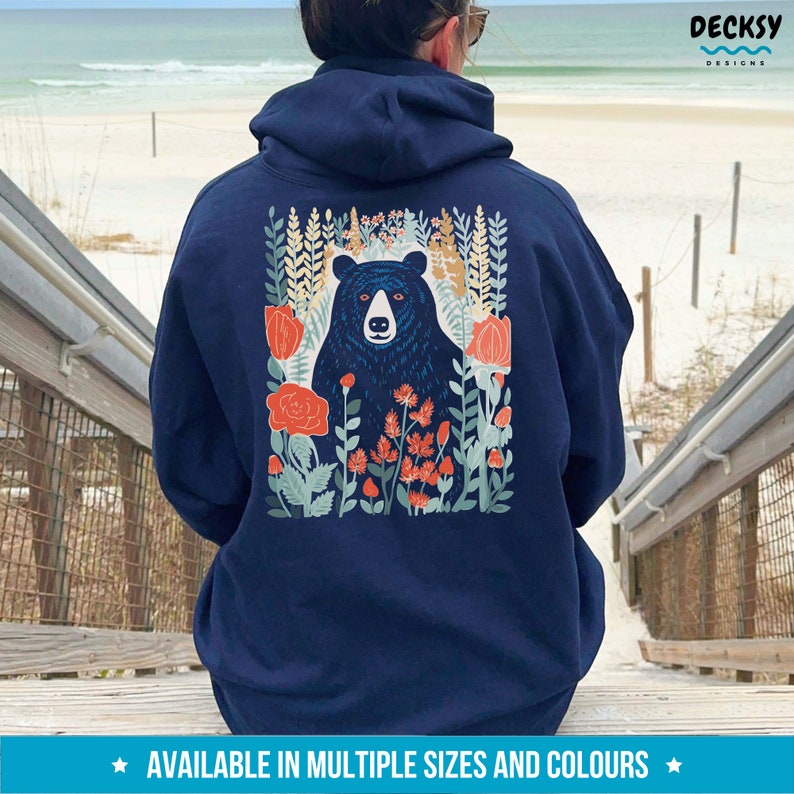 May include: Navy blue hoodie with a black bear surrounded by flowers and greenery on the back. The design is in a vintage style with red, orange, and green colors.