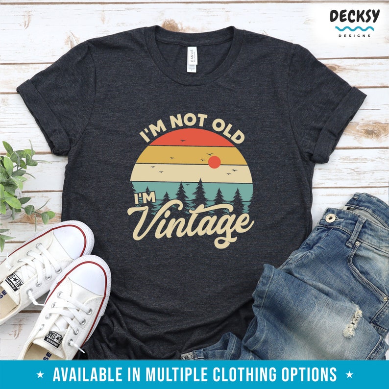 May include: A dark gray t-shirt with a vintage-style sunset graphic and the text "I'm not old, I'm vintage".