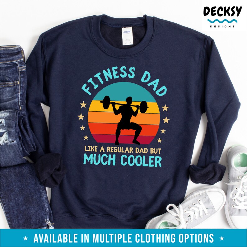 Puede incluir: Sudadera azul marino con un gr&aacute;fico retro de una persona levantando pesas. El texto "Fitness Dad" est&aacute; en azul y blanco, y el texto "Like a regular dad but much cooler" est&aacute; en azul.