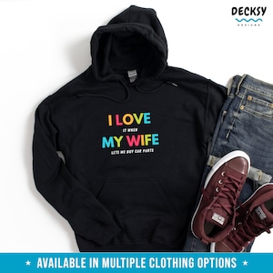 Pu&ograve; includere: Felpa con cappuccio nera con la scritta "I LOVE IT WHEN MY WIFE LETS ME BUY CAR PARTS" a colori. La felpa ha una tasca frontale e un cappuccio con coulisse. L'immagine mostra anche un paio di jeans e scarpe da ginnastica bordeaux.