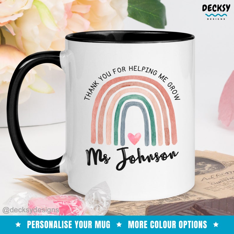 May include: White ceramic mug with a black rim and handle. The mug features a rainbow with a heart in the center and the text "Thank you for helping me grow" and "Ms. Johnson".