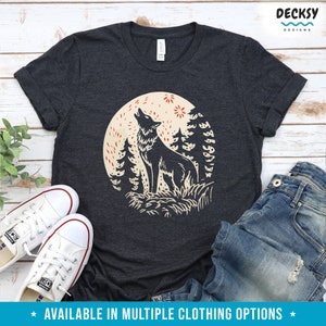 May include: A dark gray t-shirt with a graphic print of a wolf howling at the moon in a forest setting. The wolf is black and the moon is beige with red stars. The text "DECKSY DESIGNS" is in the top right corner of the image.