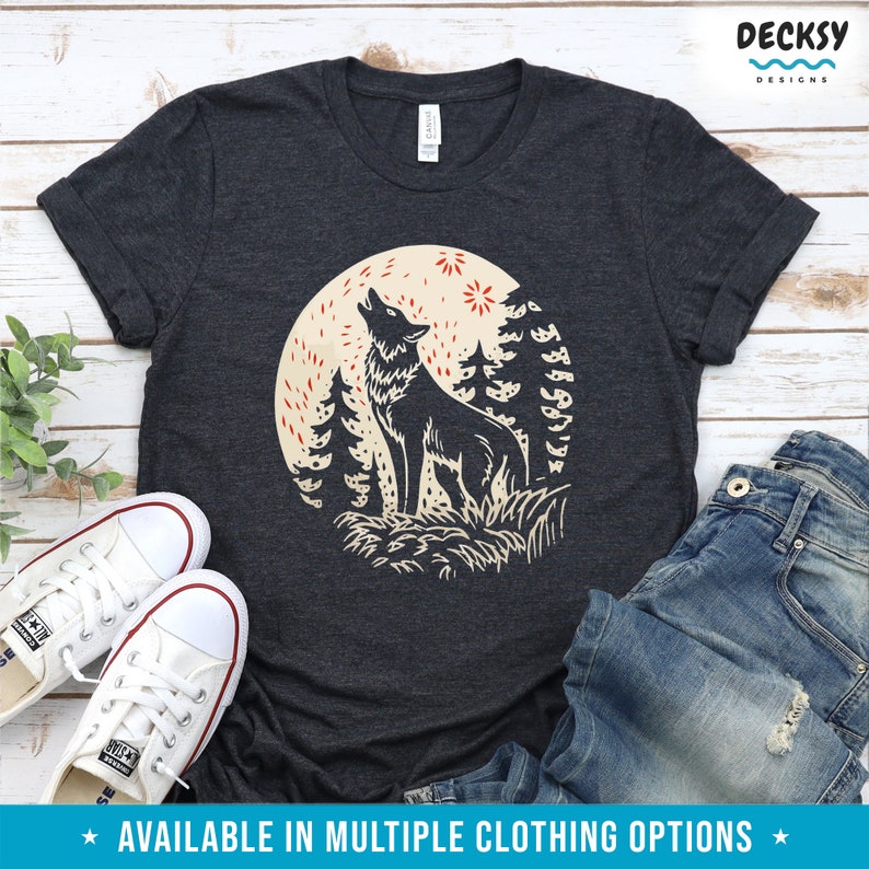 May include: A dark gray t-shirt with a graphic print of a wolf howling at the moon in a forest setting. The wolf is black and the moon is beige with red stars. The text "DECKSY DESIGNS" is in the top right corner of the image.