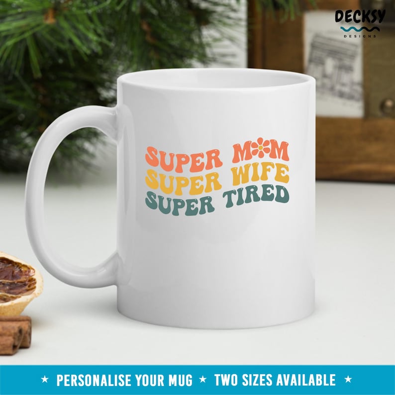 K&ouml;nnte beinhalten: Wei&szlig;e Keramiktasse mit einem Retro-Design, auf dem "SUPER MAMA SUPER FRAU SUPER M&Uuml;DE" steht.
