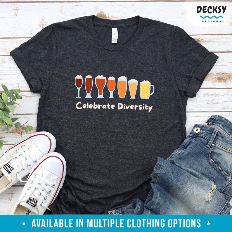 May include: Dark grey t-shirt featuring the phrase "Celebrate Diversity" above a line of beer glasses in different colours. White trainers and blue jeans are also visible. The shirt is part of a clothing range.