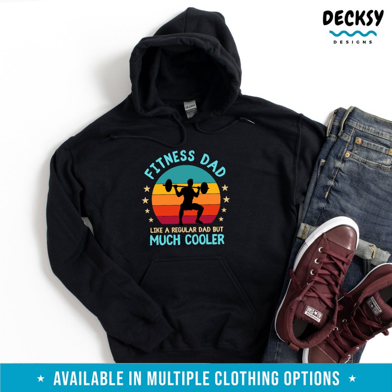 Puede incluir: Sudadera con capucha negra con un gr&aacute;fico de estilo vintage que dice "Fitness Dad" con una silueta de una persona levantando pesas. El texto debajo del gr&aacute;fico dice "Como un padre normal pero mucho m&aacute;s cool."