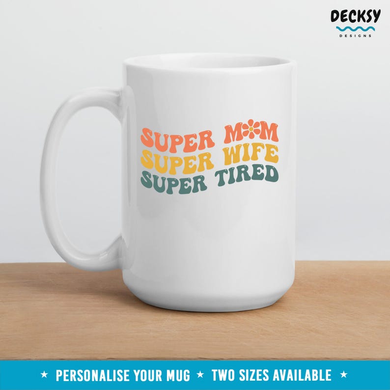 K&ouml;nnte beinhalten: Wei&szlig;e Keramiktasse mit dem Text "SUPER MOM SUPER WIFE SUPER TIRED" in einer Retro-Schriftart mit einem Blumendesign. Der Text ist in Orange-, Gelb- und Gr&uuml;nt&ouml;nen gehalten.