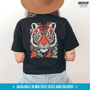 Puede incluir: Camiseta negra con un gr&aacute;fico de la cara de un tigre rodeado de elementos florales naranja y grises. El texto "Girl" es visible en la manga derecha.