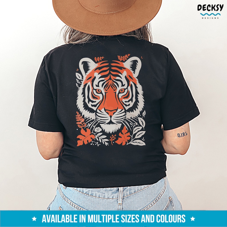 Puede incluir: Camiseta negra con un gr&aacute;fico de la cara de un tigre rodeado de elementos florales naranja y grises. El texto "Girl" es visible en la manga derecha.