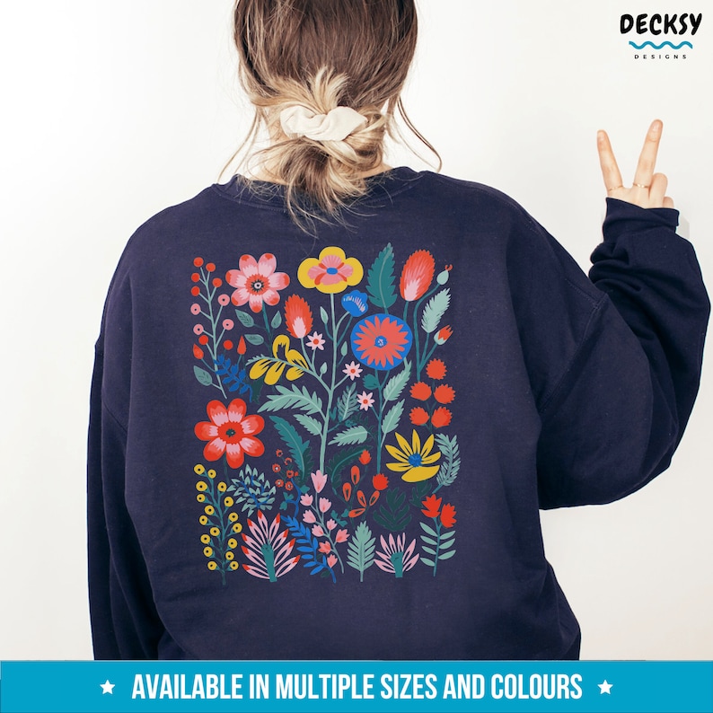 May include: A navy blue sweatshirt with a colorful floral design on the back. The design features a variety of flowers, leaves, and stems in shades of red, yellow, pink, green, and blue.