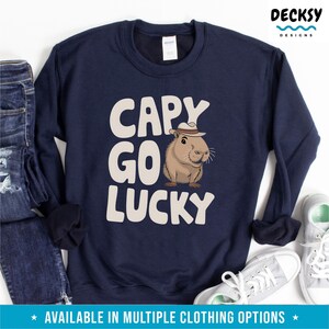 May include: Navy blue sweatshirt with a white capybara wearing a hat and the text "Capy Go Lucky".