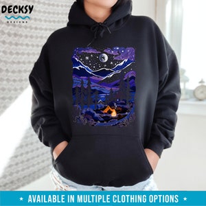May include: A black hoodie with a colorful illustration of a nighttime camping scene. The illustration features a tent, a campfire, a moon, stars, and a mountain range.