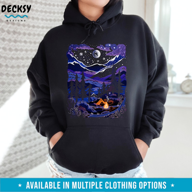 May include: A black hoodie with a colorful illustration of a nighttime camping scene. The illustration features a tent, a campfire, a moon, stars, and a mountain range.