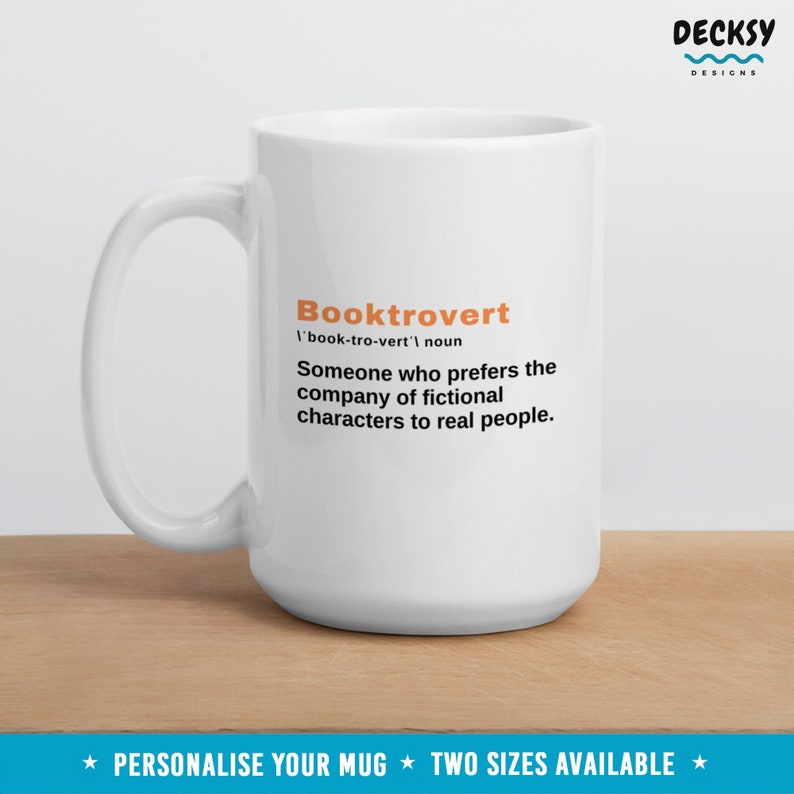 May include: White ceramic mug with a black and orange design. The mug features the word "Booktrovert" defined as "Someone who prefers the company of fictional characters to real people."