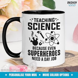 Puede incluir: Taza de cerámica blanca con borde y asa negros. La taza tiene un diseño negro que dice "TEACHING SCIENCE BECAUSE EVEN SUPERHEROES NEED A DAY JOB". El diseño también incluye un vaso de precipitados, un tubo de ensayo y un átomo.